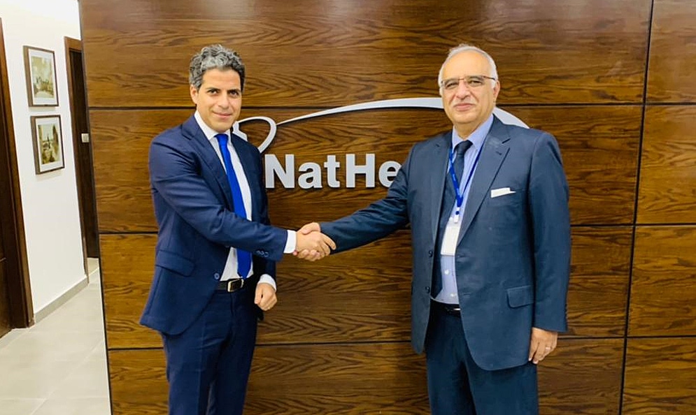 two men shaking hands on a deal in front of a logo on a wall