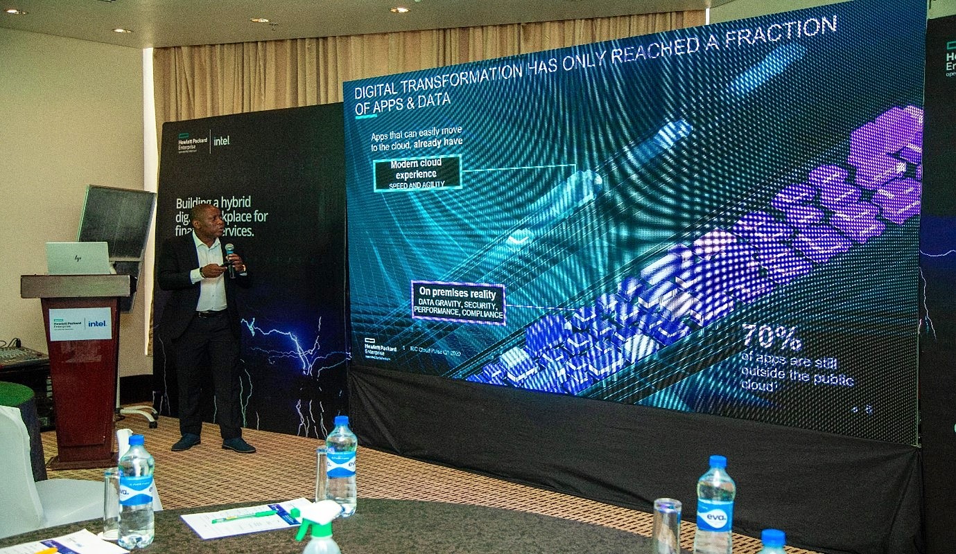 a man presents with a mic in front of a large digital projection screen