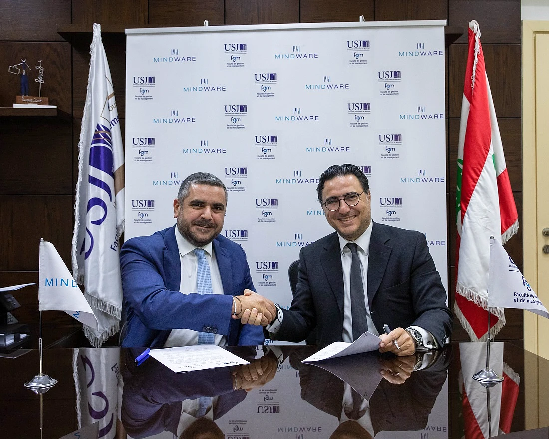 Two men are seen sitting at a desk signing an agreement