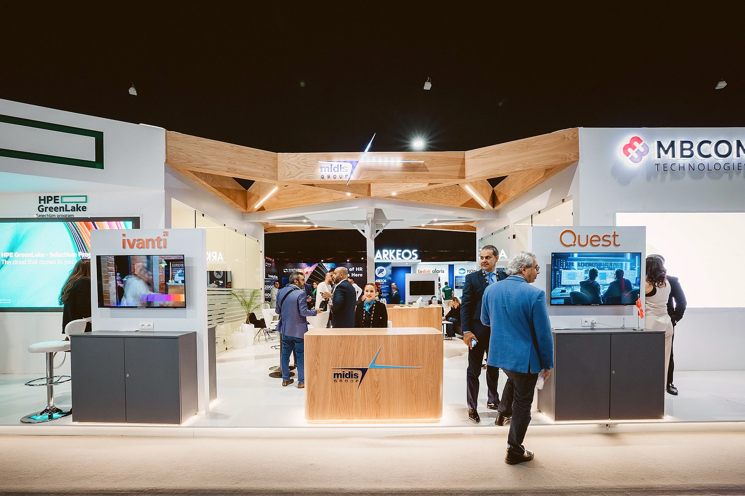 two exhibition booths are seen from the front of the stand. In the centre a woman sits at a welcome desk with the Midis Group logo on it