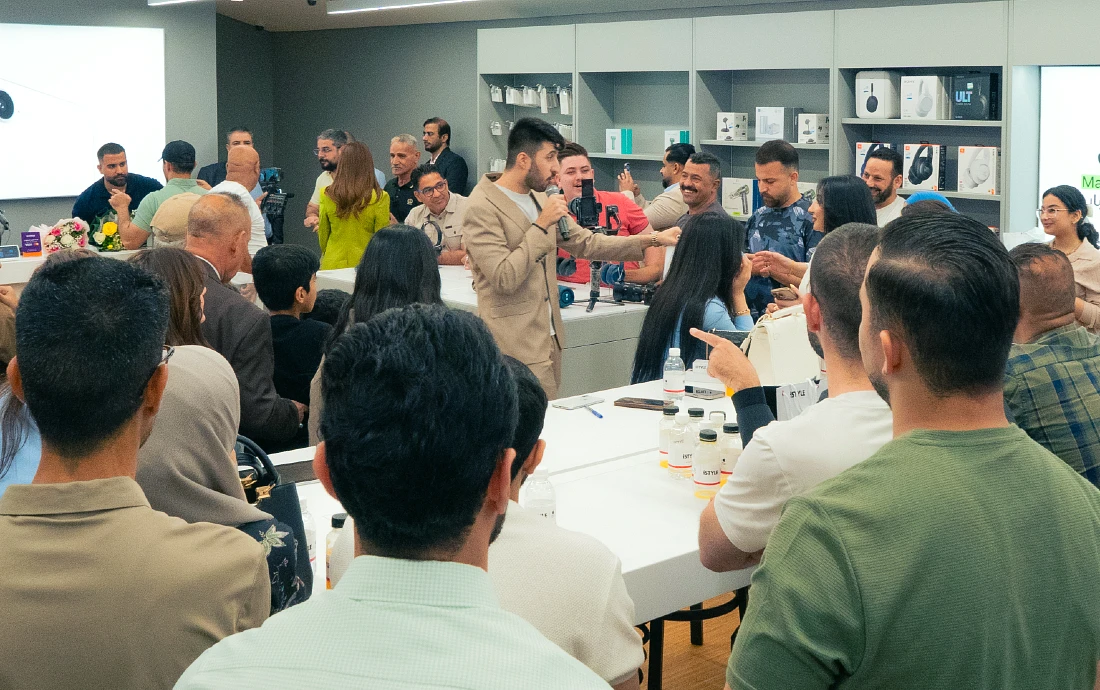 a man is seen speaking into a mic surrounded by many Apple fans in a hi tech store interior