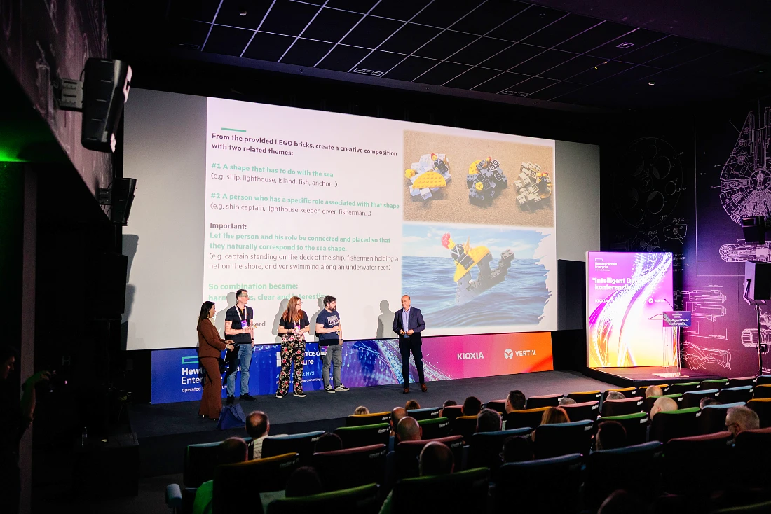 Five people on a presentation stage at a hi tech event with a powerpoint screen seen behind them