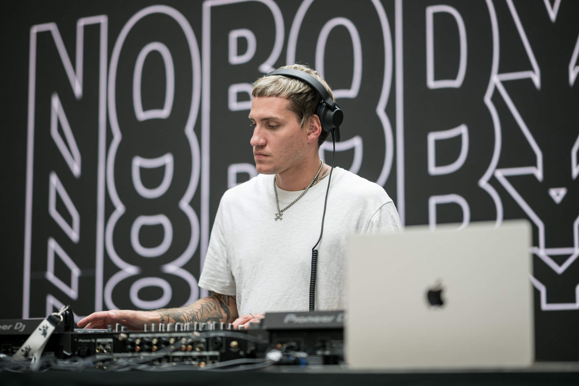 a DJ plays music at a hi-tech store opening. He is wearing earphones and an Apple laptop is in the foreground