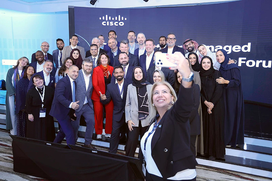 Un groupe de collègues est vu sur scène lors d'un événement high-tech, avec une personne au-devant prenant un selfie.