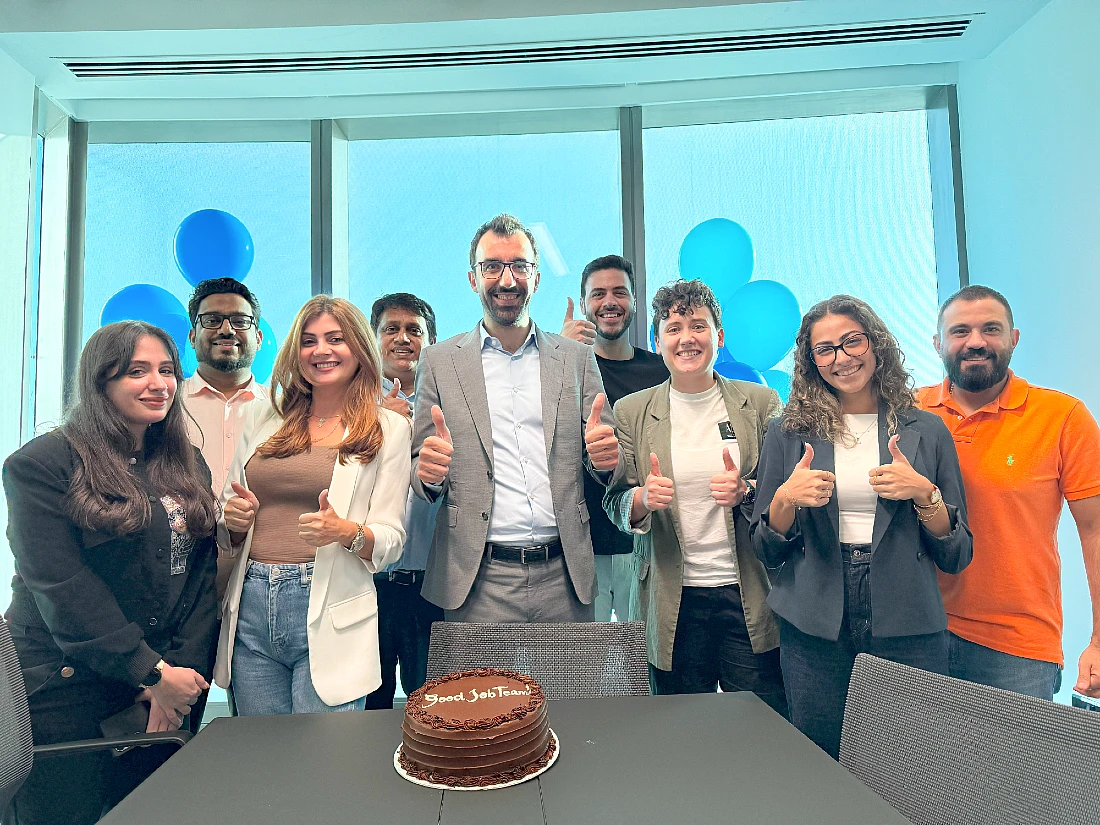 Un groupe de collègues souriant, dans un bureau, un gâteau posé devant eux sur une table avec l'inscription « Bravo à l'équipe » en guise de cerise sur le gâteau.