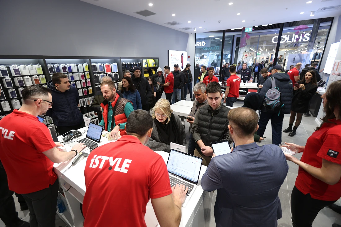 Scène animée lors de l'ouverture d'une boutique high-tech : clients et employés discutent des produits Apple proposés.