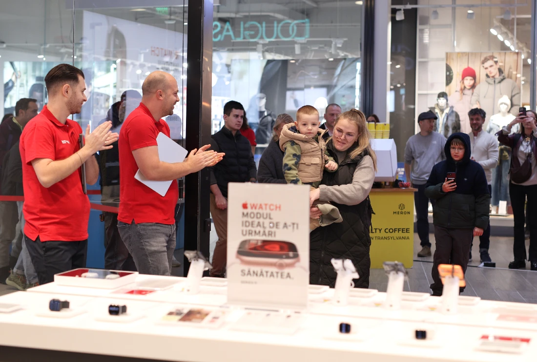 Deux employés du magasin applaudissent une femme et un jeune enfant qui entrent dans un magasin high-tech lors de son ouverture.