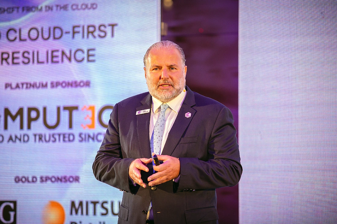 a man in a suit speaks to an audience at a hi tech event