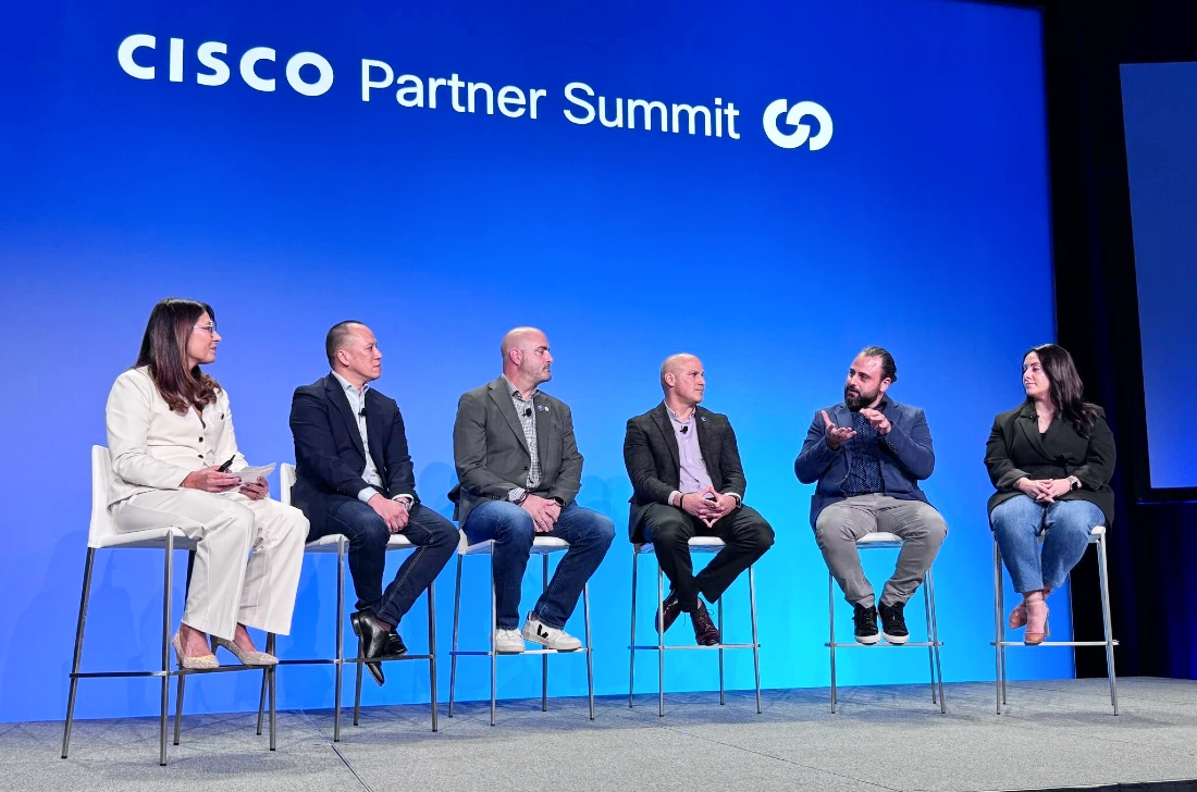 Six people are seen on stage at a hi tech event with one of them talking and gesturing