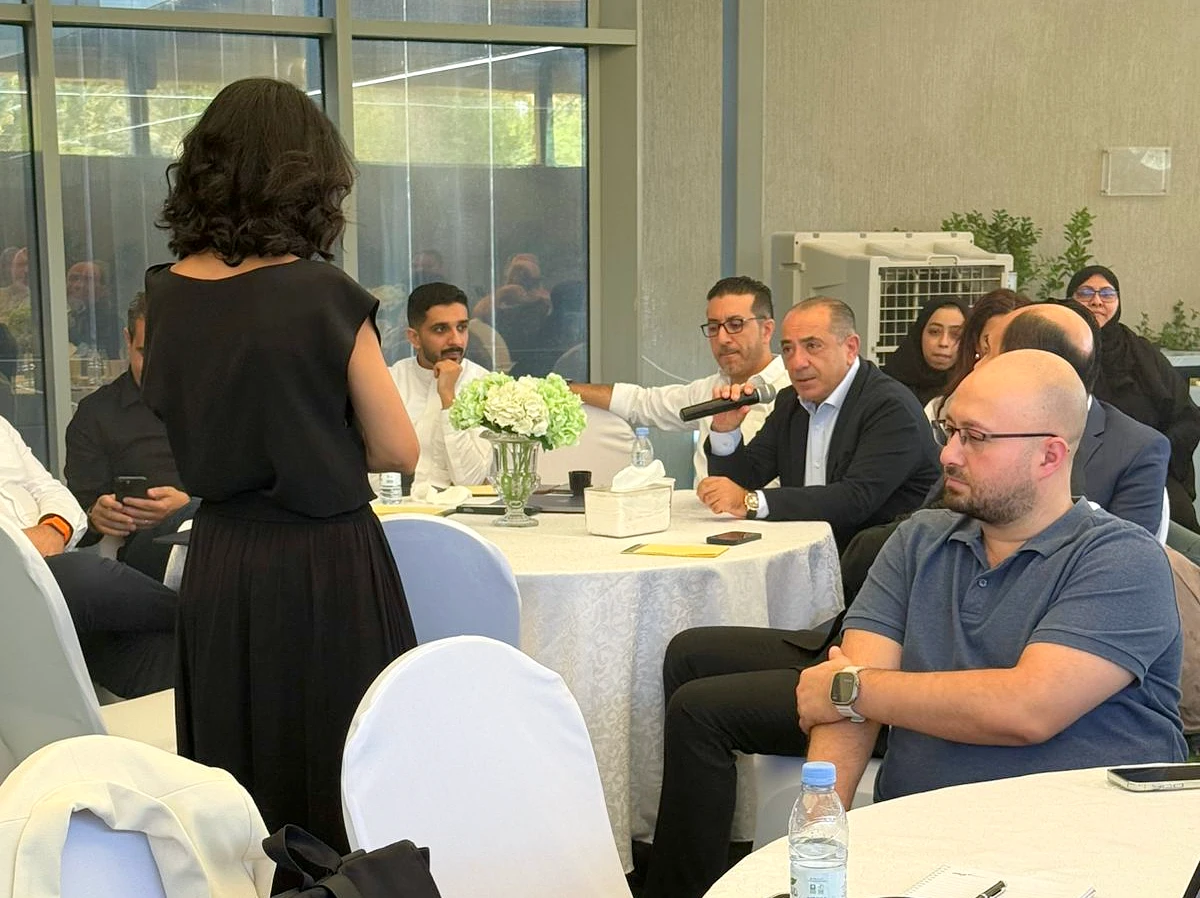 a man is seen holding a microphone and talking as he sits among a group of people in a boardroom