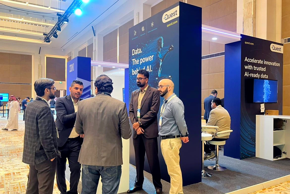 five men talking together in front of a booth at a hi tech exhibition
