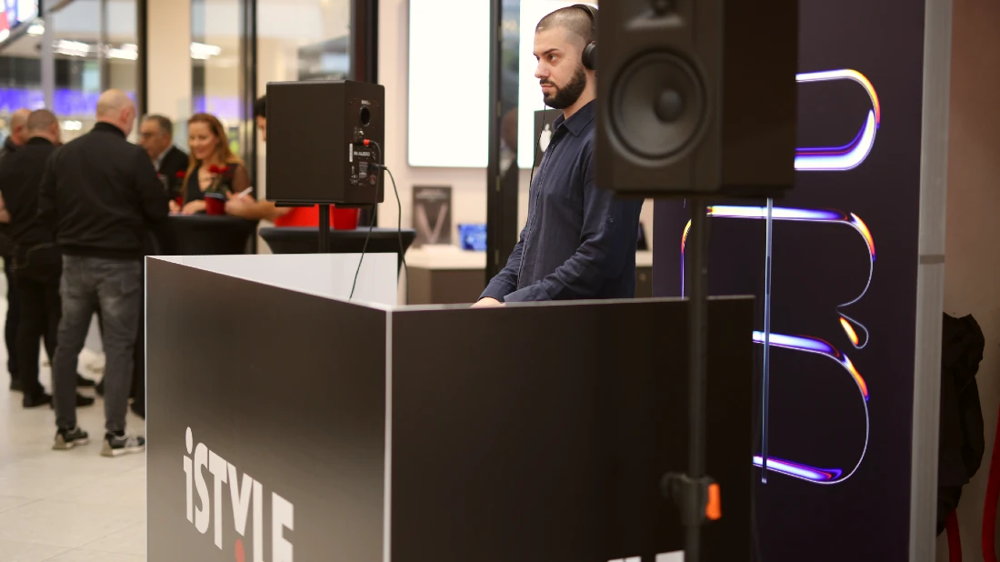 Un DJ mixe depuis sa cabine devant une boutique high-tech.