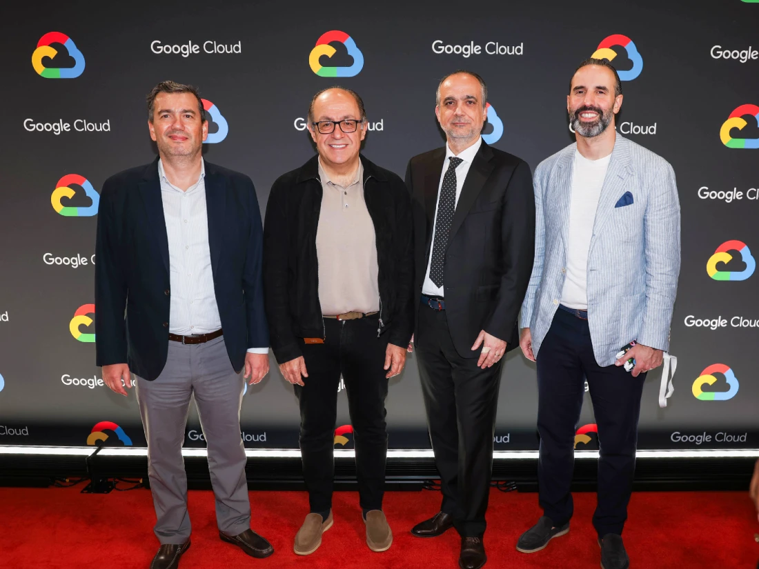 Four men are seen smiling in a group photo with a colourful background behind them with the words Google Cloud prominent.  