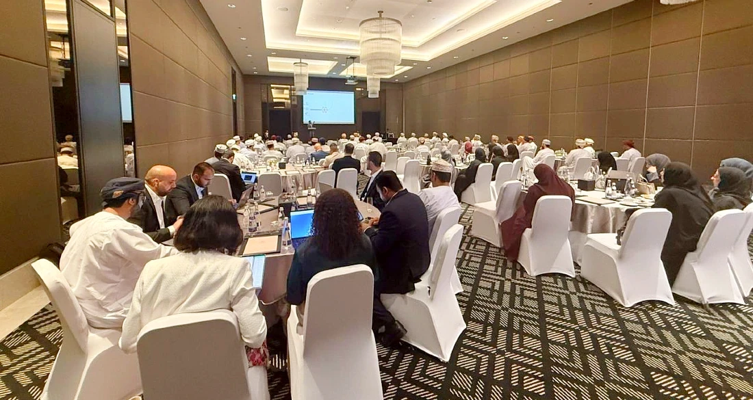 Delegates at a hi tech event are seen at tables in a large room with a screen at the far end